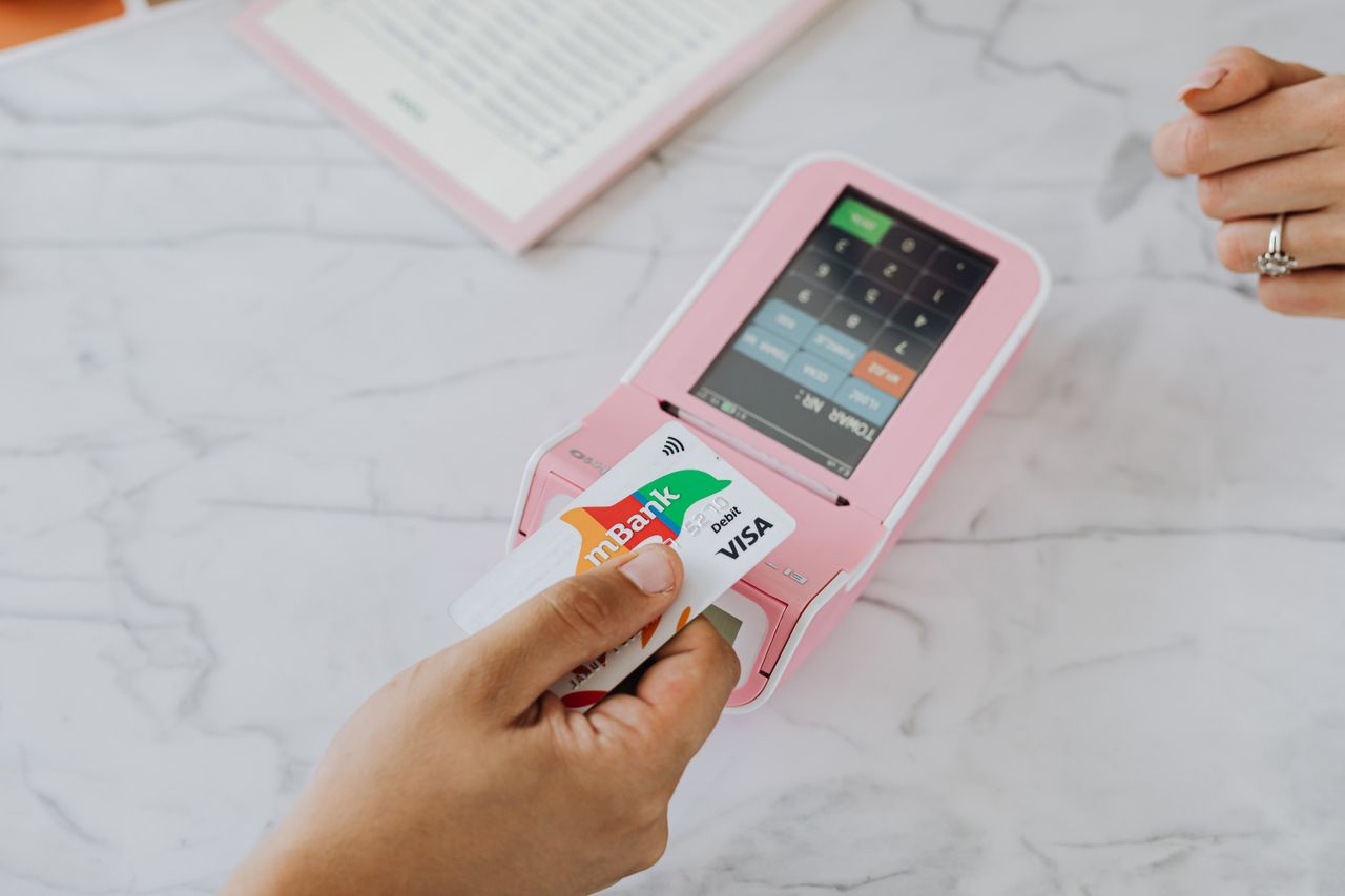 about-us Hand using a contactless card on a pink POS terminal for a wireless transaction.